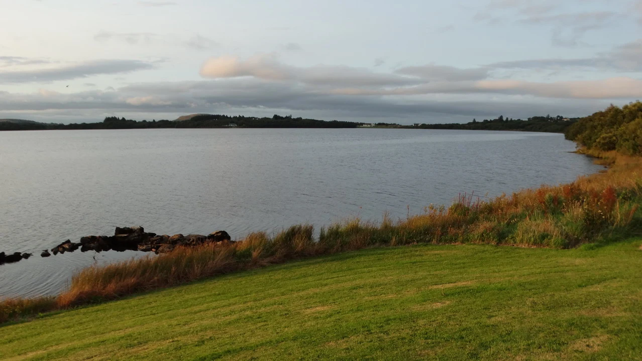 Un paesaggio lacustre in Irlanda al tramonto con vegetazione lussureggiante lungo la riva.