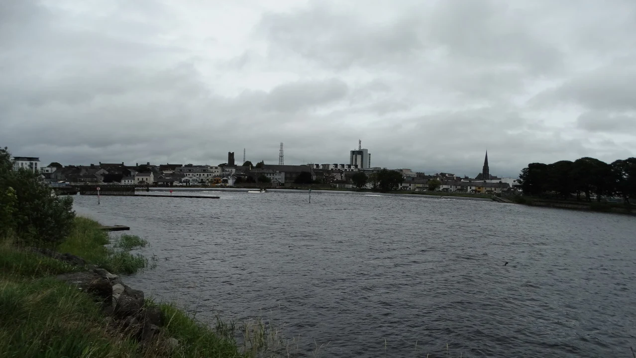Panorama di una città irlandese lungo un fiume sotto un cielo coperto.