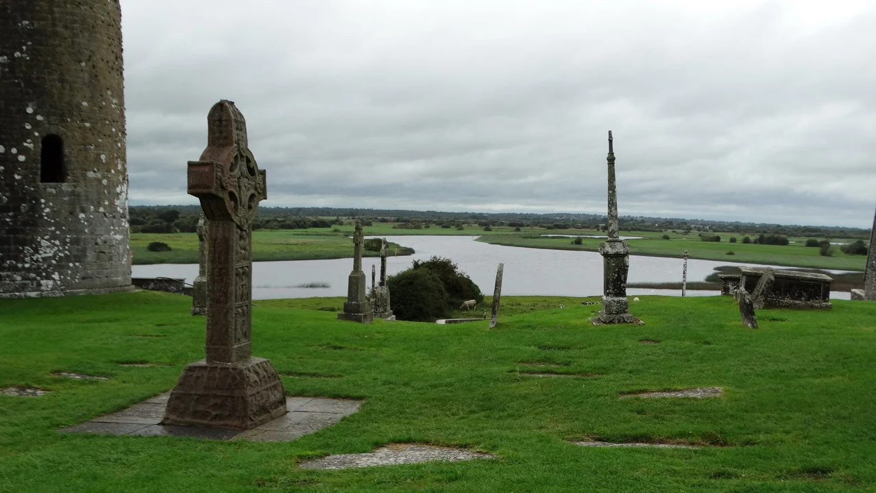 Resti di un sito monastico in Irlanda si stagliano su un terreno erboso con un lago.