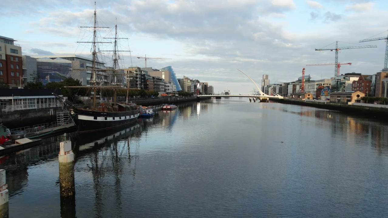 Il fiume Liffey scorre attraverso il centro di Dublino con imbarcazioni storiche e edifici moderni sullo sfondo.