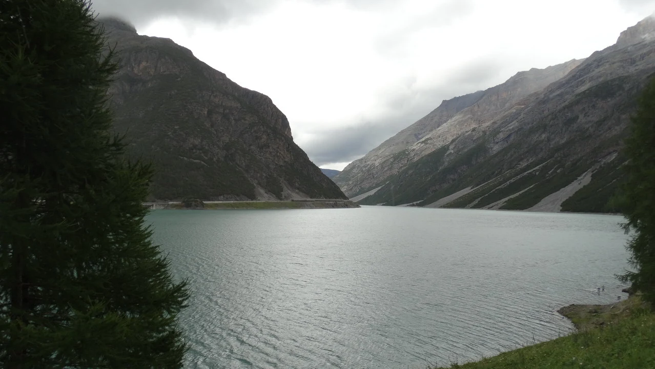 Paesaggio alpino di un lago circondato da montagne imponenti sotto un cielo coperto.