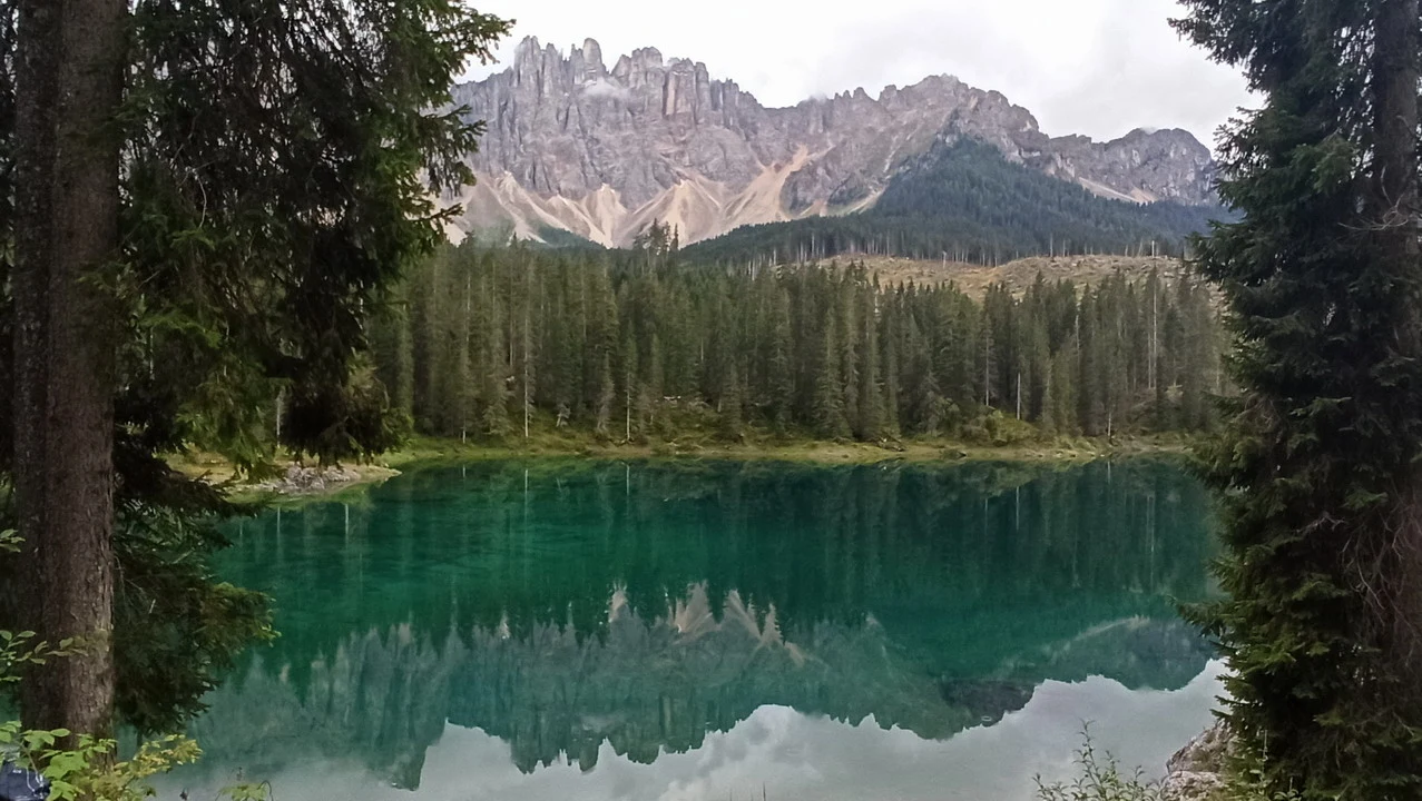 Lago alpino smeraldo riflette montagne innevate e foreste verdi.