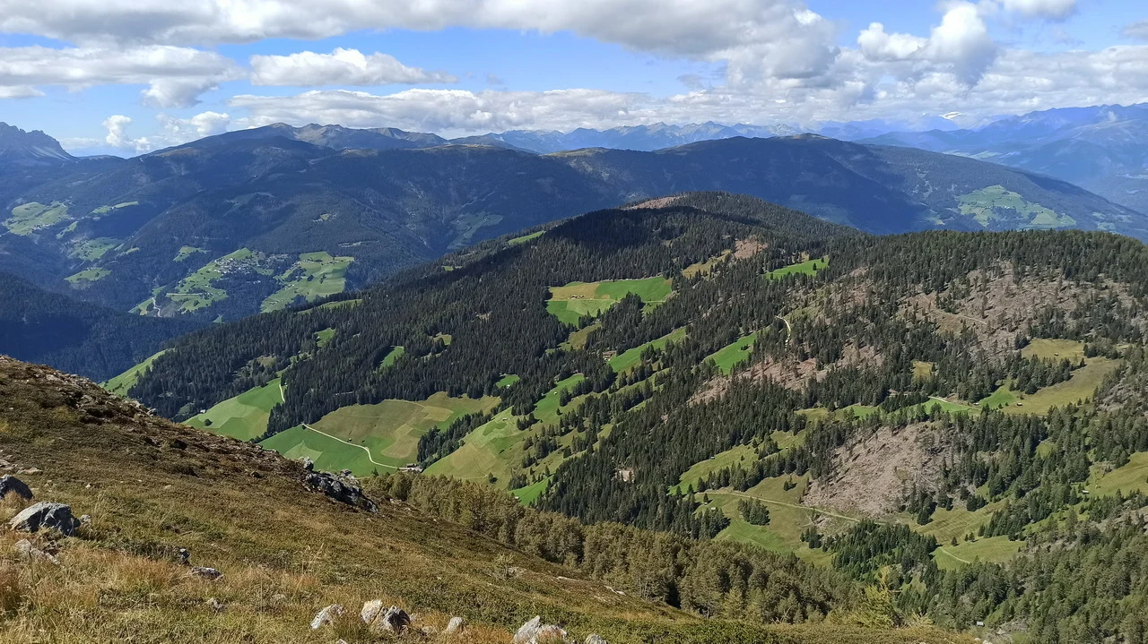 Cavalieri attraversano le montagne delle Alpi italiane in una vasta pianura verde.