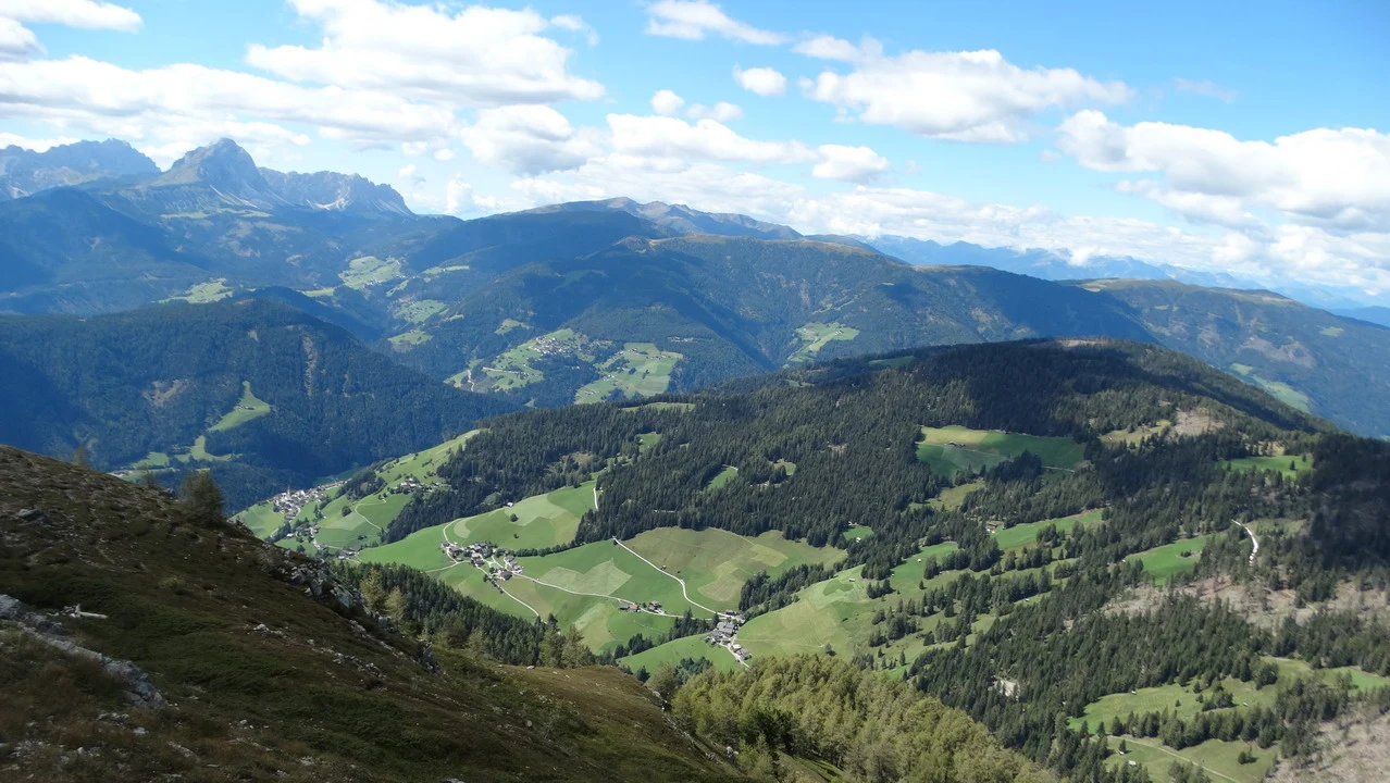 Cavalieri attraversano le Alpi italiane in un paesaggio montano verdeggiante.