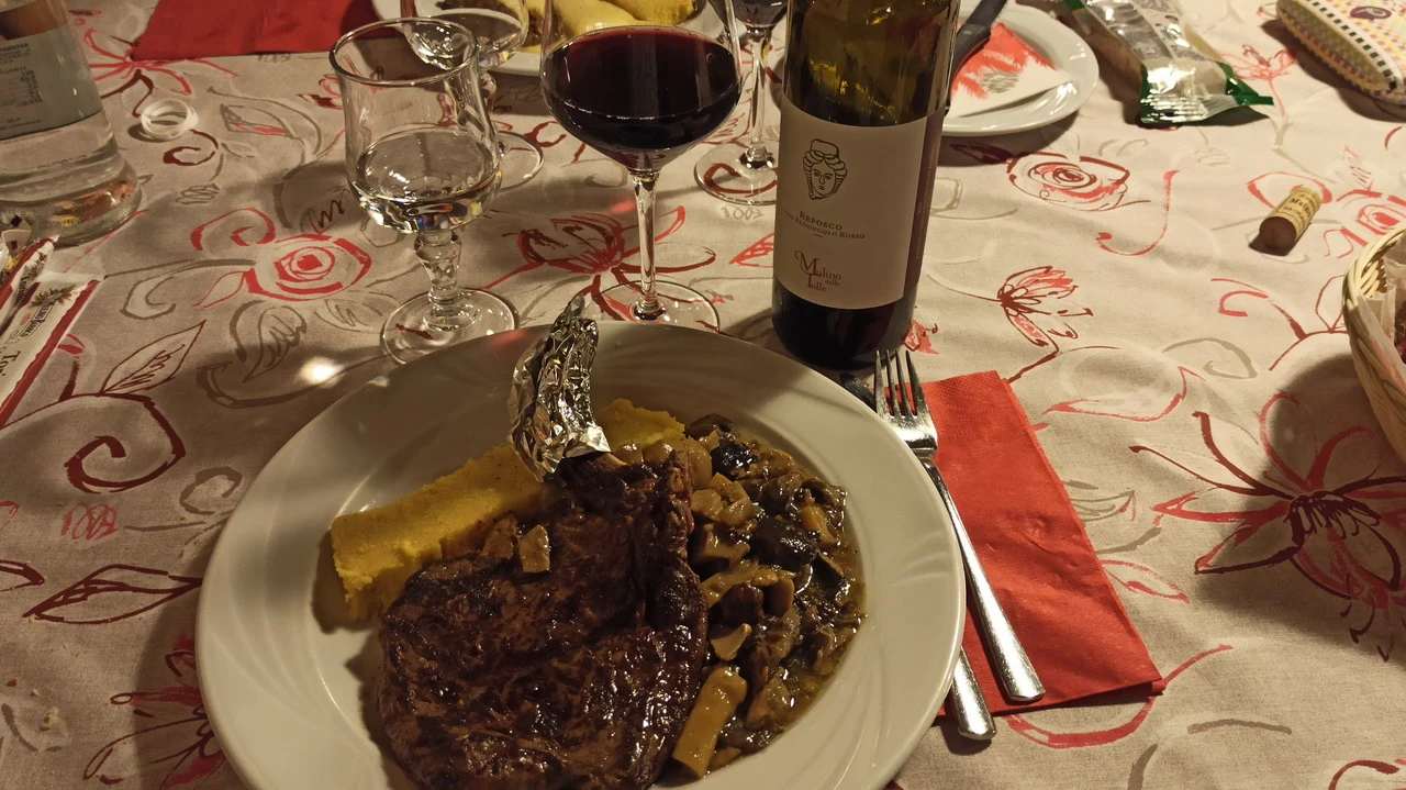 Cena con costata di cervo e vino in un ambiente rustico.