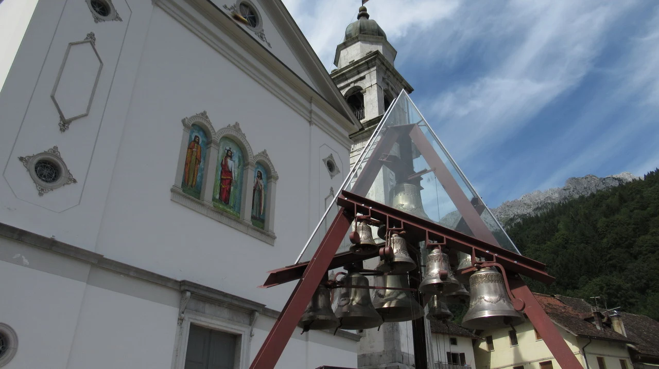 Facciata di una chiesa con campane in un paesaggio alpino italiano.