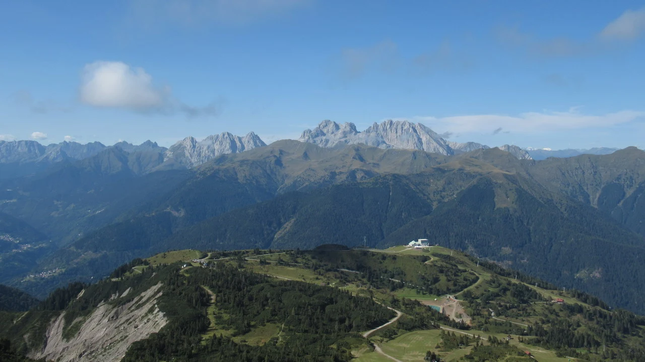 Panorama vasto delle Alpi italiane con pendii boscosi e cime rocciose.