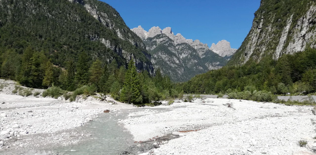 Cavallo in una valle alpina con montagne rocciose sullo sfondo.