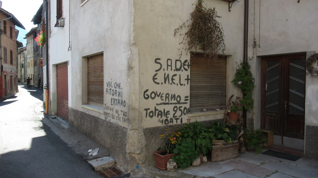 Cavalieri attraversano una strada stretta in un paesaggio alpino italiano.