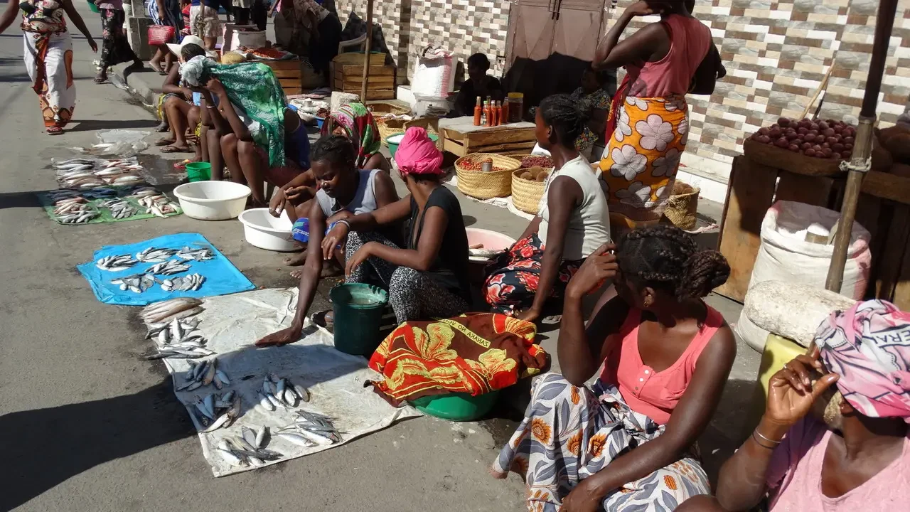 Persone sedute in un mercato all'aperto con merci esposte sul terreno.
