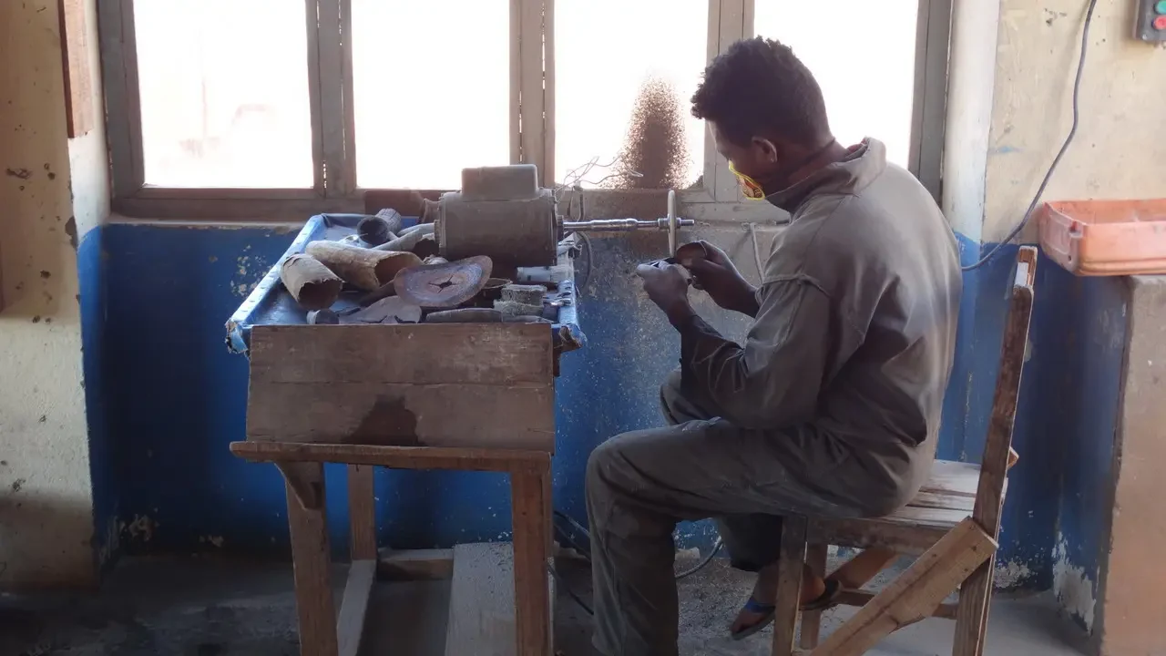 Un uomo lavora su pezzi di legno in un ambiente interno.