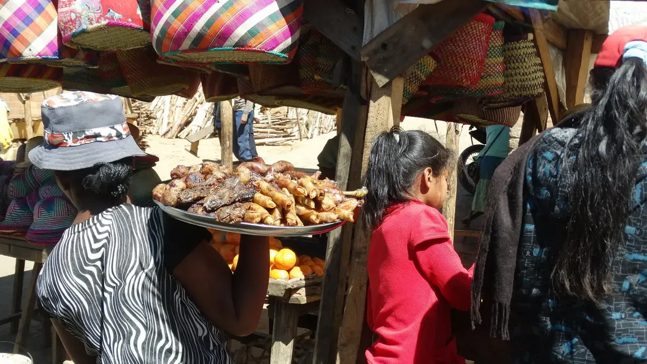 Persone osservano carne grigliata esposta in un mercato locale di Madagascar.