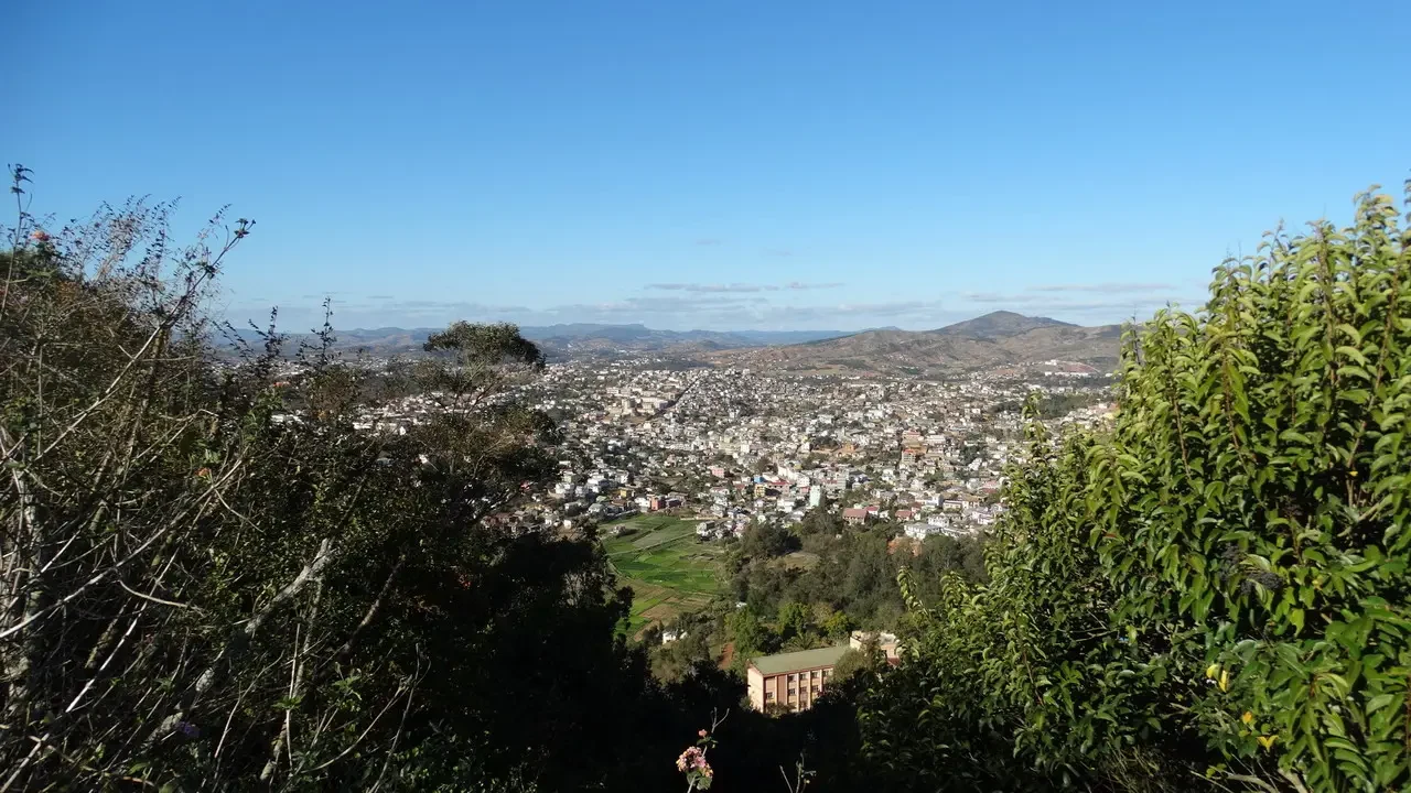Vista panoramica di una città che si estende su colline ondulate sotto un cielo sereno.