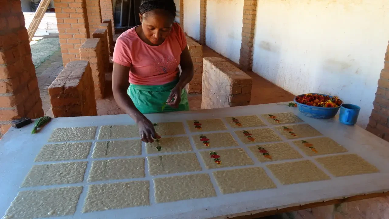 Una donna lavora su una superficie con piccoli oggetti colorati in un ambiente esterno.