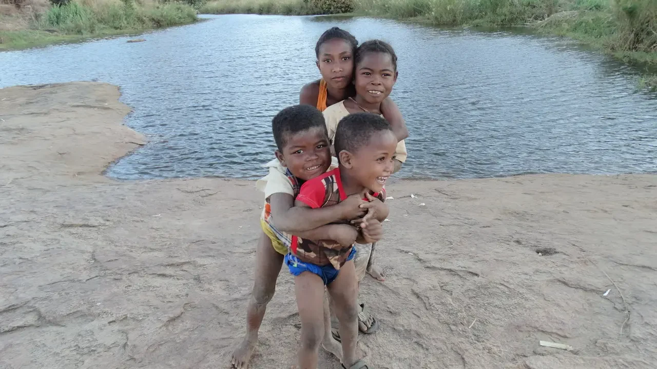 Bambini sorridono vicino a un corso d'acqua in Madagascar.