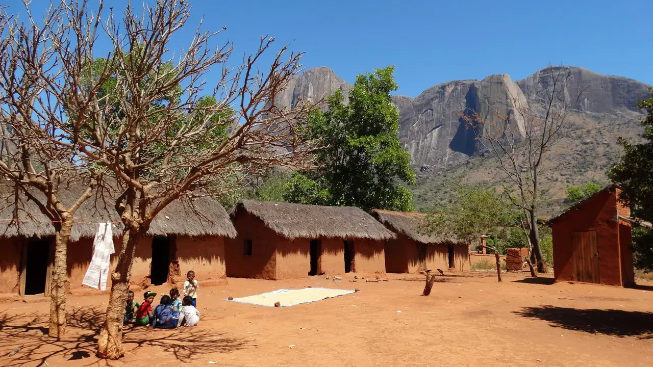 Paesaggio rurale con case in terra cotta e montagne rocciose di Madagascar sullo sfondo.
