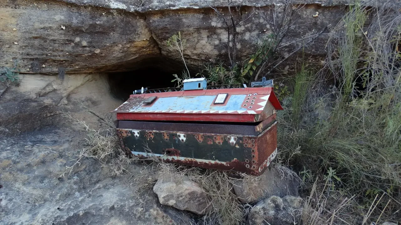 Una struttura arrugginita giace davanti a un ingresso roccioso in un ambiente secco.