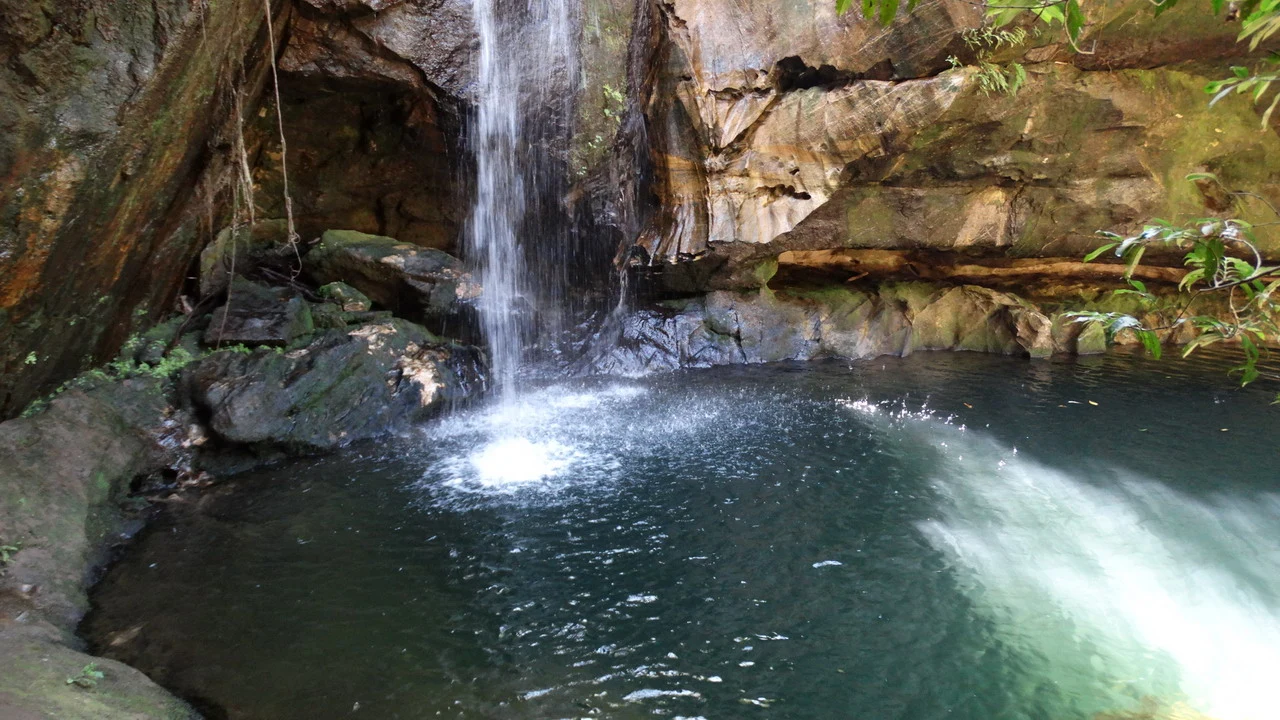 Una cascata d'acqua scende su rocce verdi e scure in una gola naturale.