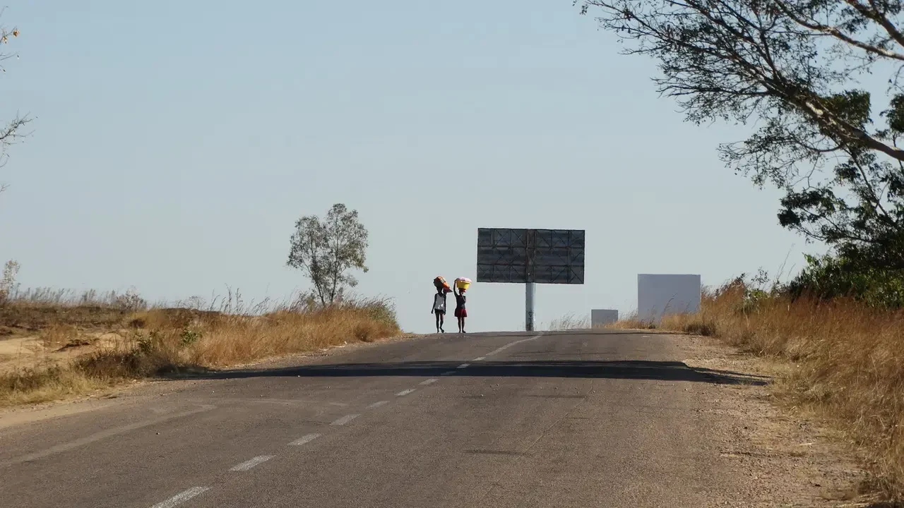 Due persone camminano su una strada di campagna sotto un cielo chiaro.