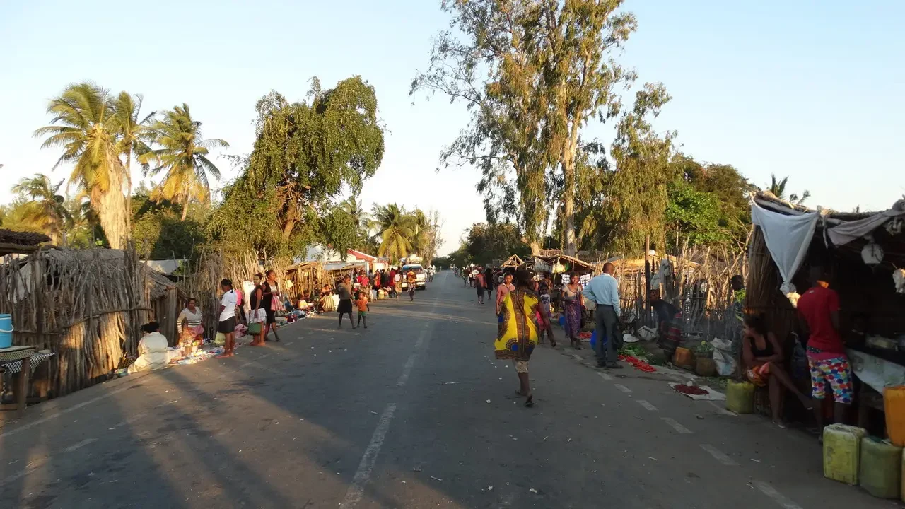 Una strada sterrata in un villaggio di Madagascar con persone che camminano lungo il bordo.