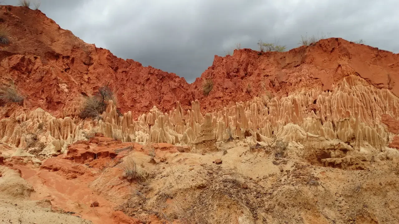 Formazioni rocciose rosse e erose dominano il paesaggio arido di Madagascar sotto un cielo coperto.