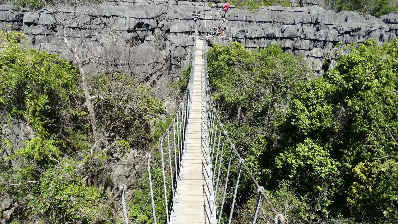 Una passerella in legno attraversa un paesaggio roccioso e boscoso di Madagascar.