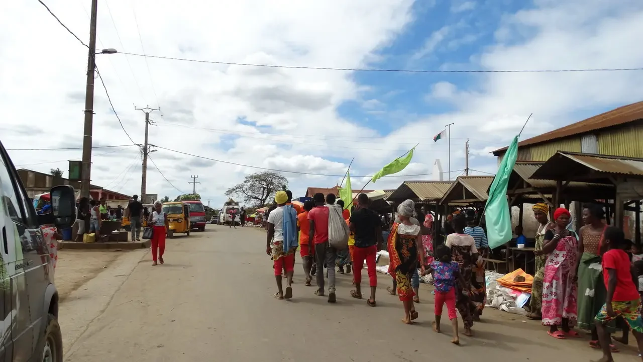 Un gruppo di persone attraversa una strada in un villaggio di Madagascar con bancarelle lungo il lato.