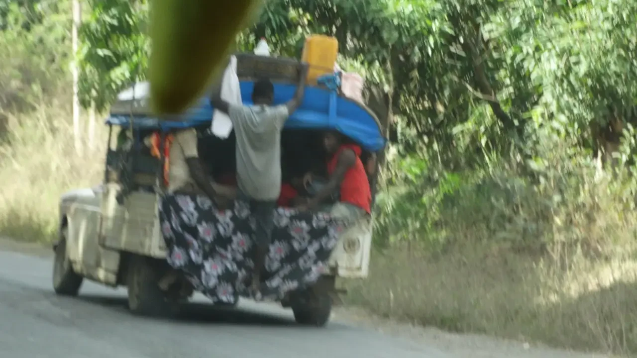 Un veicolo percorre una strada rurale con persone a bordo.