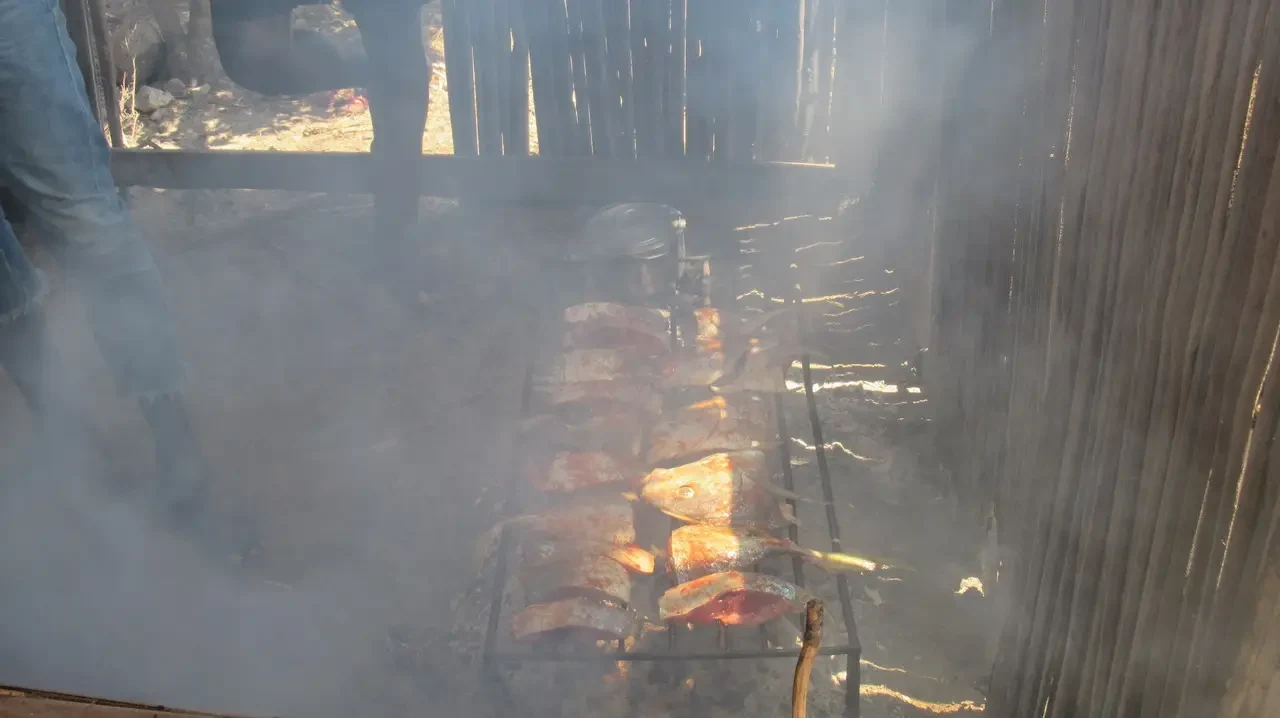 Persone cucinano cibo sulla griglia sopra le braci in un ambiente rustico.