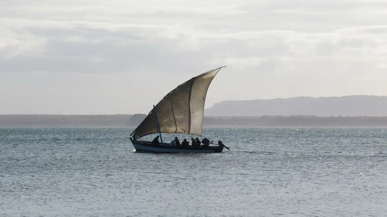 Una barca con una vela naviga sull'acqua calma.