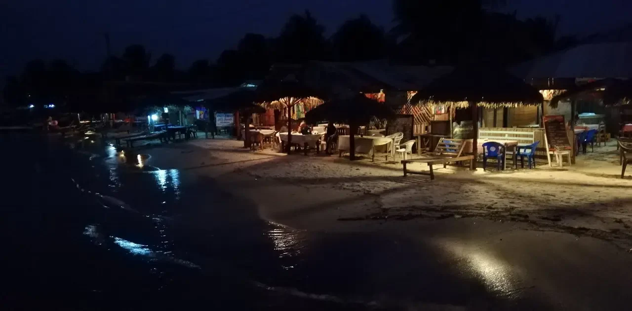 Ristorante all'aperto con tavoli illuminati di luce calda lungo la riva.
