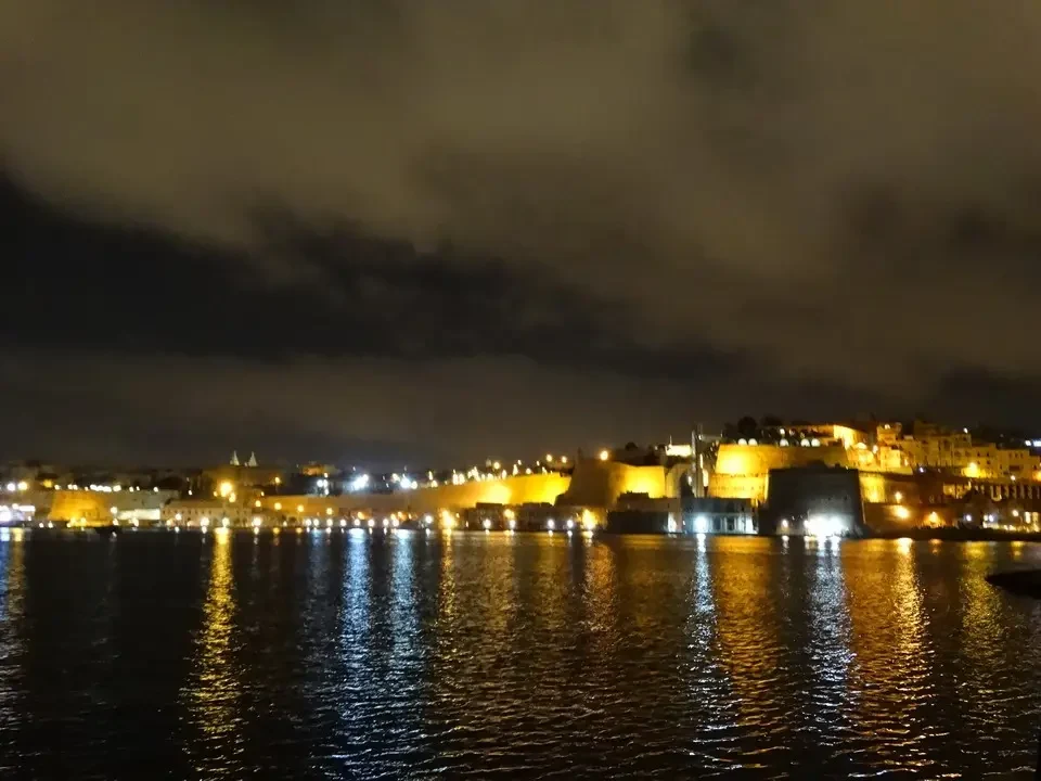 La città di Valletta è illuminata di notte riflessa sull'acqua.