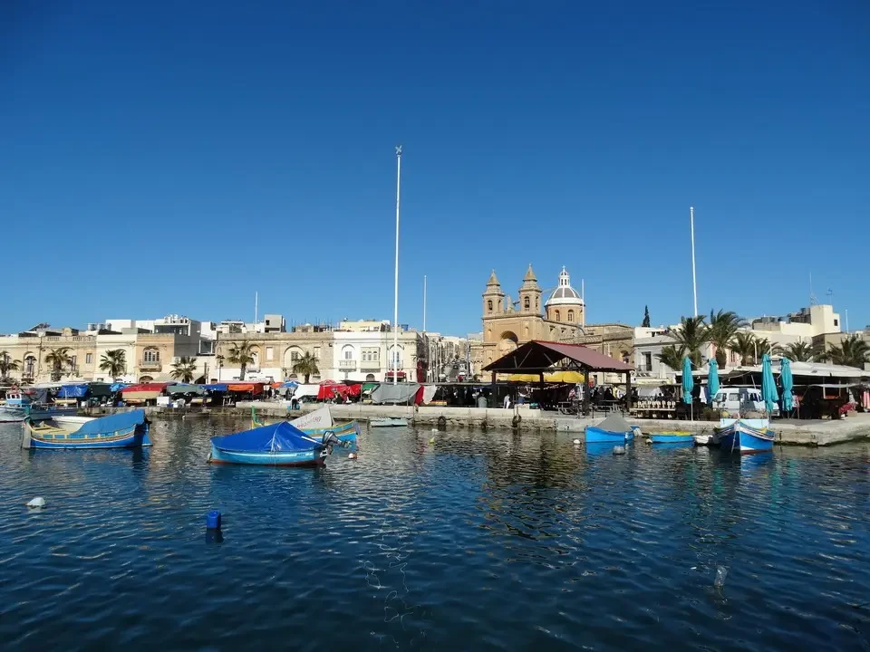 Una veduta panoramica del porto di Marsaxlokk con barche ormeggiate sotto il cielo azzurro.