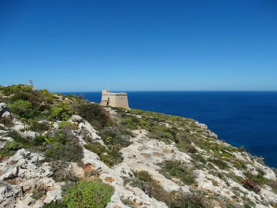 Una piccola struttura in pietra si trova su una scogliera rocciosa di Gozo con il mare aperto visibile.