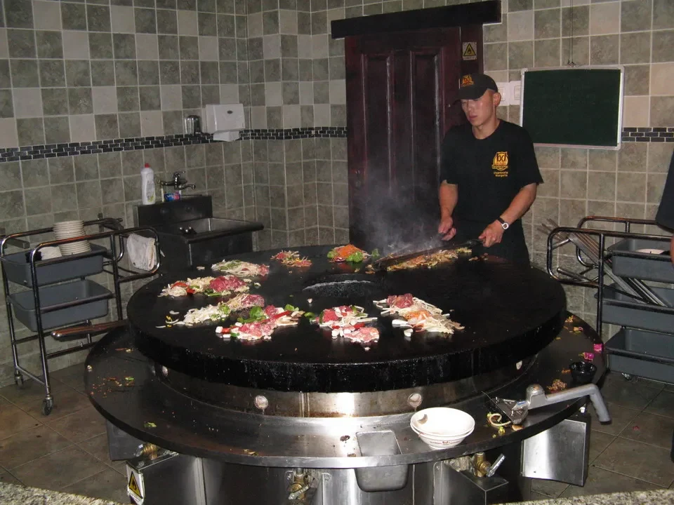 Un uomo cucina carne su una griglia in un ambiente interno.