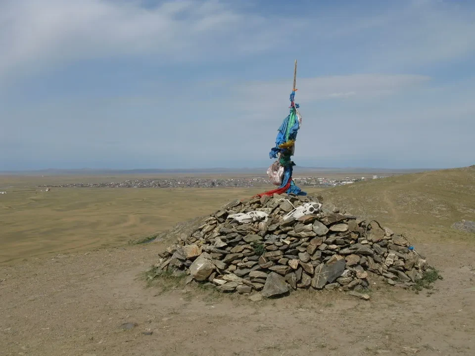 Una pila di pietre con tessuti colorati si stagliano contro il cielo aperto della Mongolia.