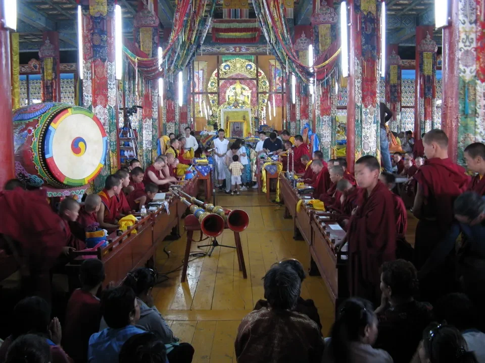 Interno di un monastero mongolo con decorazioni vivaci e persone sedute in una sala comunitaria.