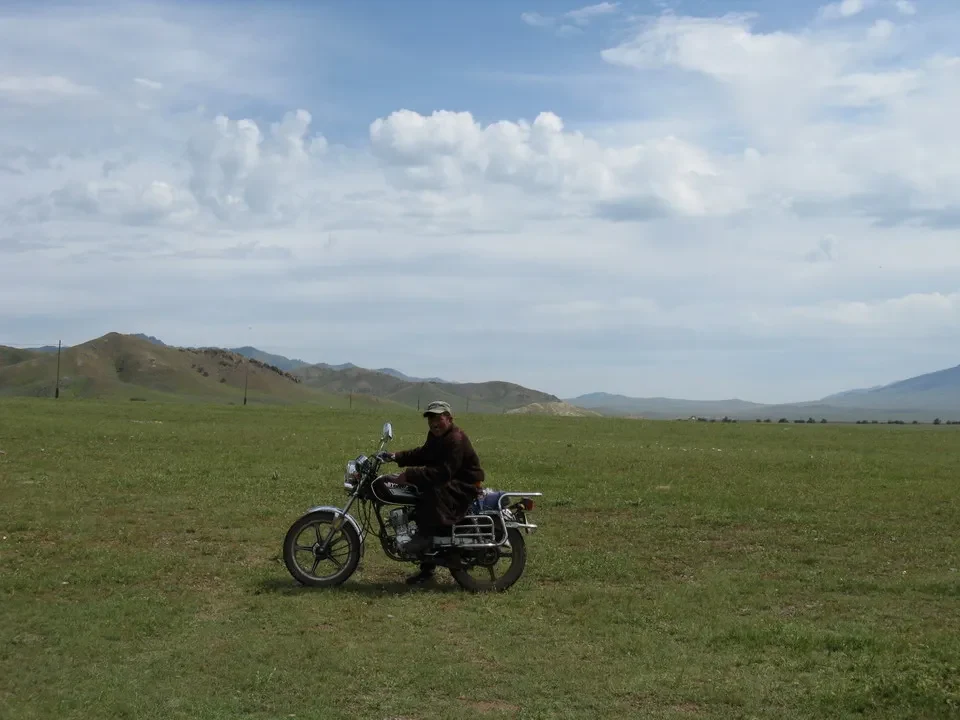 Un nomade cavalca una motocicletta in un vasto paesaggio di prato mongolo.