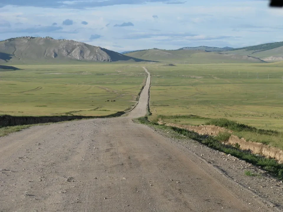 A strada sterrata attraversa un vasto paesaggio di praterie e colline in Mongolia.
