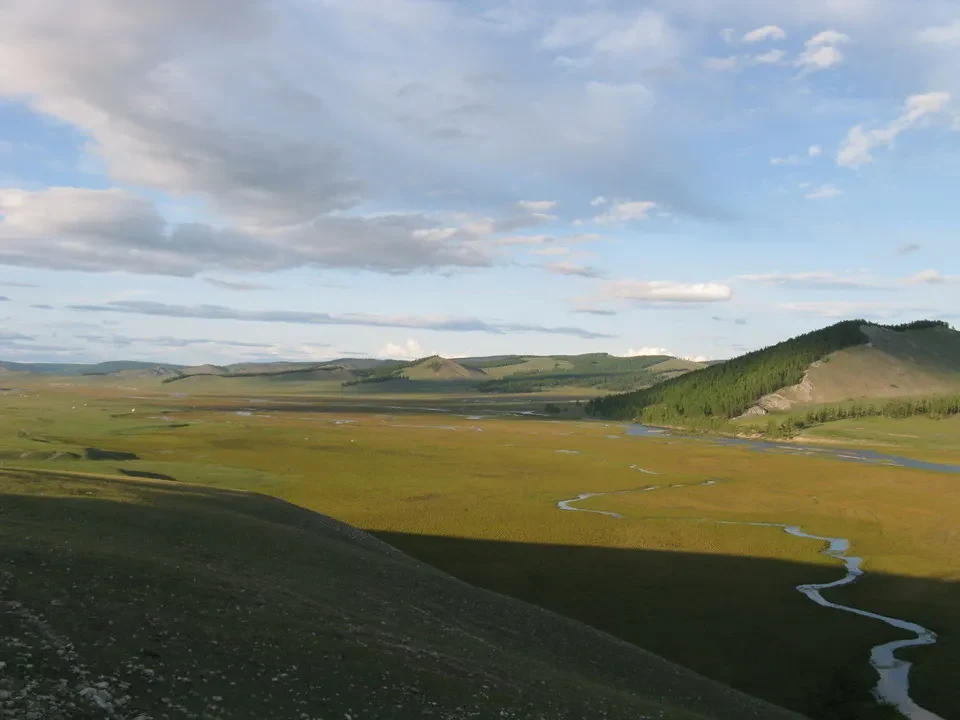Paesaggio vasto della Mongolia con un fiume che scorre attraverso la pianura erbosa.