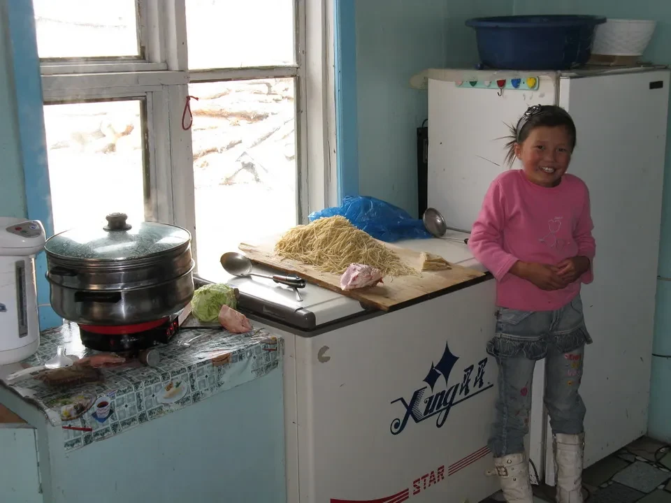 Una bambina sorride davanti a una cucina rustica in Mongolia.