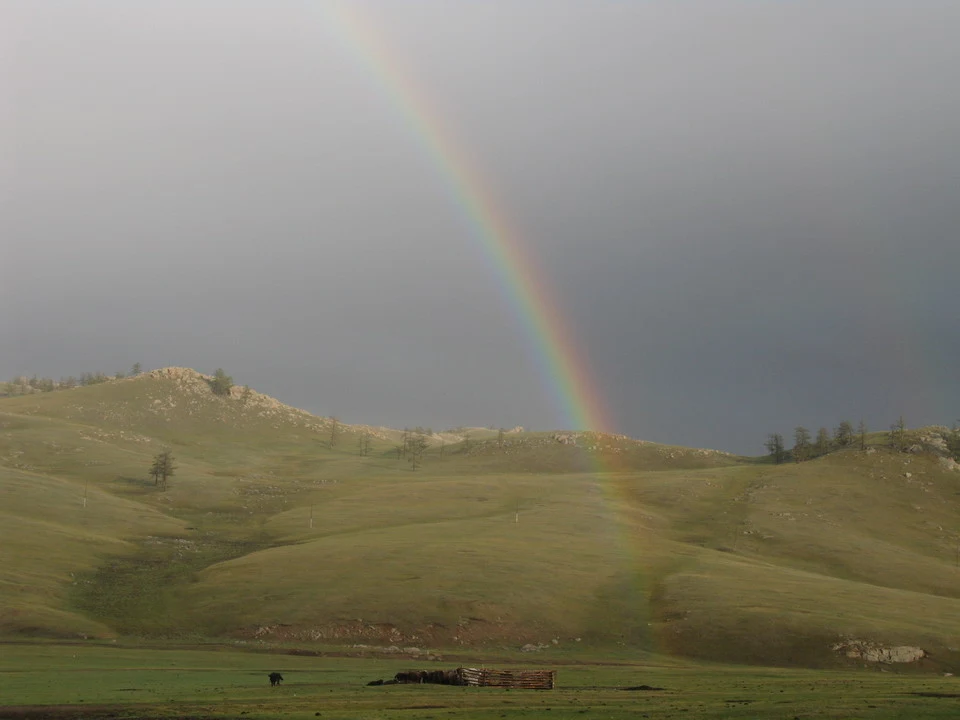 Un arcobaleno si estende sopra un paesaggio collinare in Mongolia.