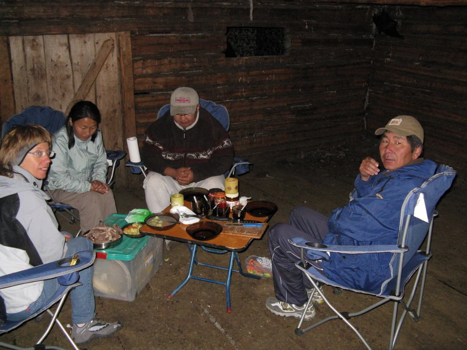 Un gruppo di persone è seduto attorno a un tavolo all'interno di una struttura rustica in Mongolia.
