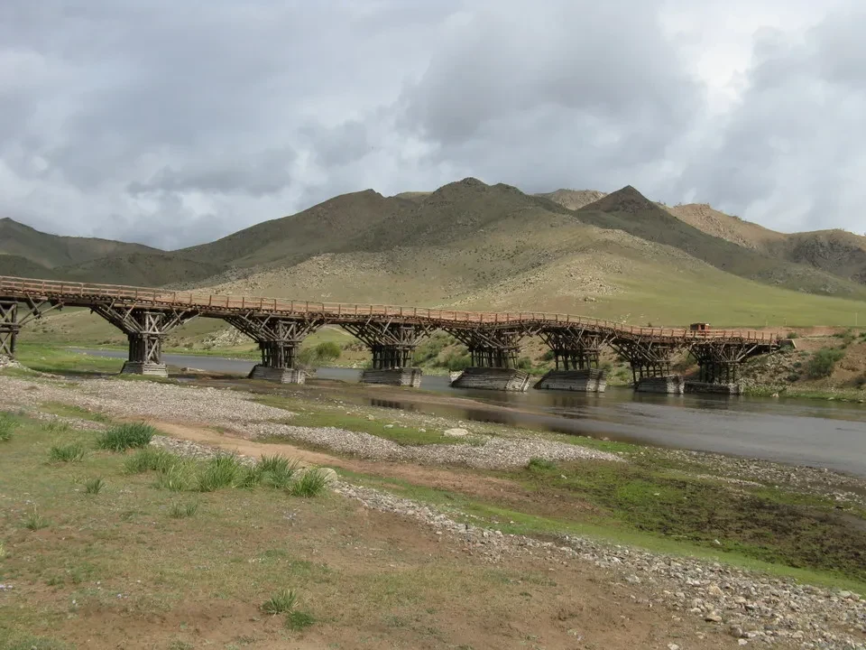 Un ponte in legno attraversa un fiume in una paisagna mongola.
