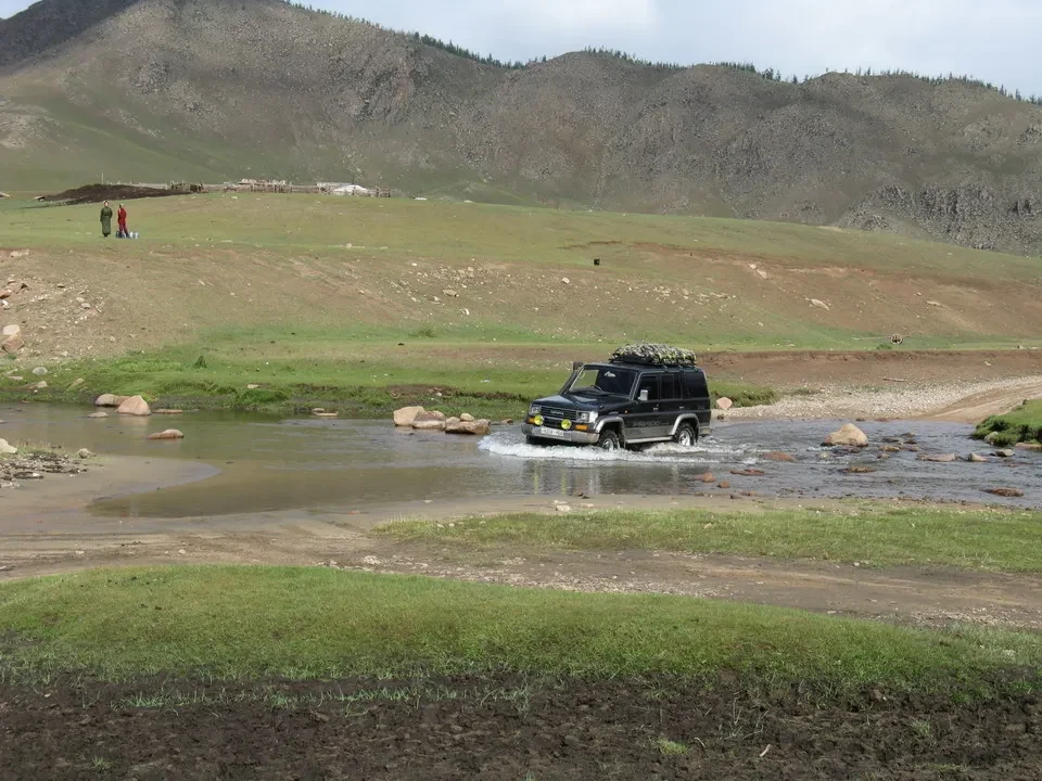 Un SUV attraversa un fiume poco profondo in un paesaggio mongolo.