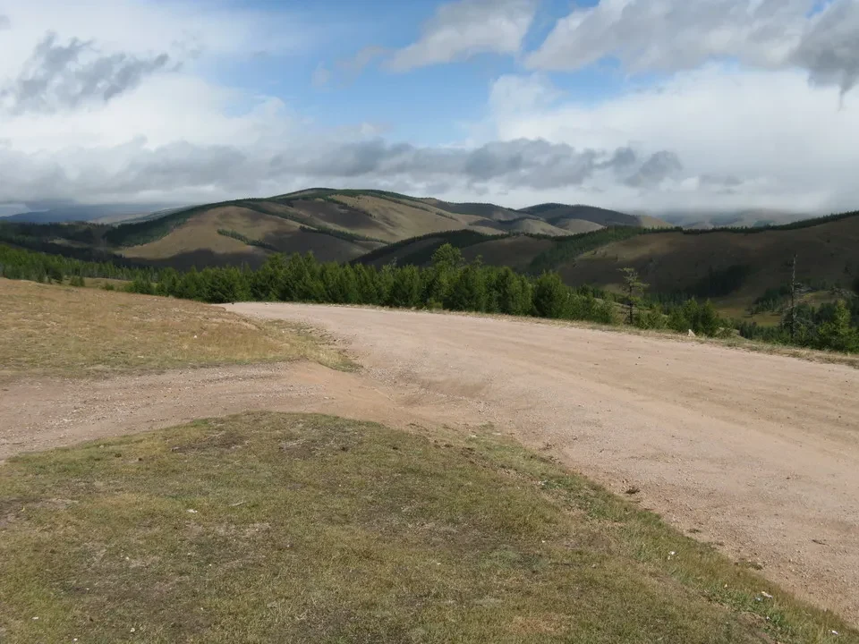 Paesaggio montano in Mongolia con un sentiero sterrato e vegetazione bassa.
