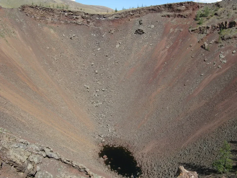 Una vasta e ripida collina terrosa con una depressione scura al centro.