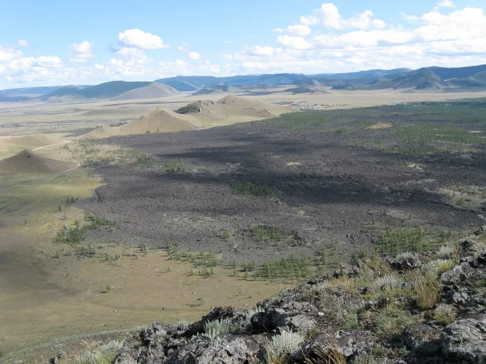 Paesaggio vasto della Mongolia con colline ondulate e vegetazione bassa in primo piano.