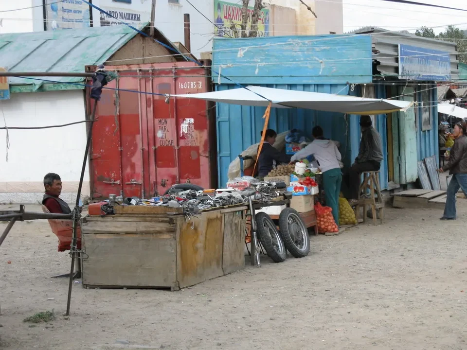 Un mercato all'aperto in Mongolia mostra bancarelle di merci e persone che interagiscono con la merce.