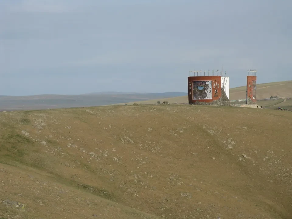 Paesaggio ondulato della steppa mongola con due strutture verticali in lontananza.